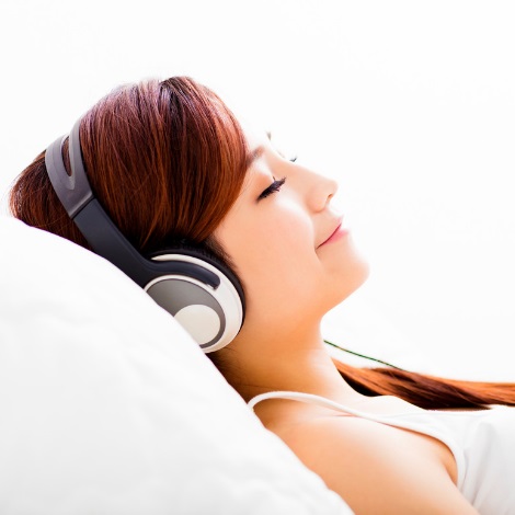 Woman wearing headphones laying back on pillow with eyes closed, relaxing.