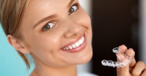 woman smiling and holding up a clear aligner